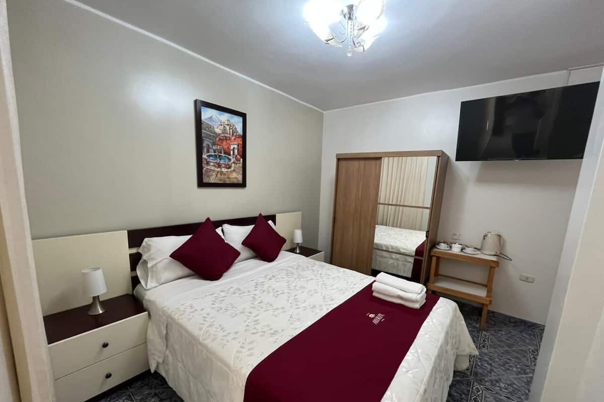 A neatly arranged hotel room with a bed, bedside table, lamp, and a television mounted on the wall.