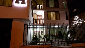Um hotel com um grande letreiro em formato de 'H', entrada por portão e uma varanda visível no andar superior.