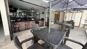 Uma área de estar ao ar livre com mesa e cadeiras, um balcão com banquetas e um ventilador de teto.