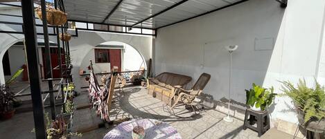 A covered patio area with wicker furniture, a crocheted table, and potted plants.
