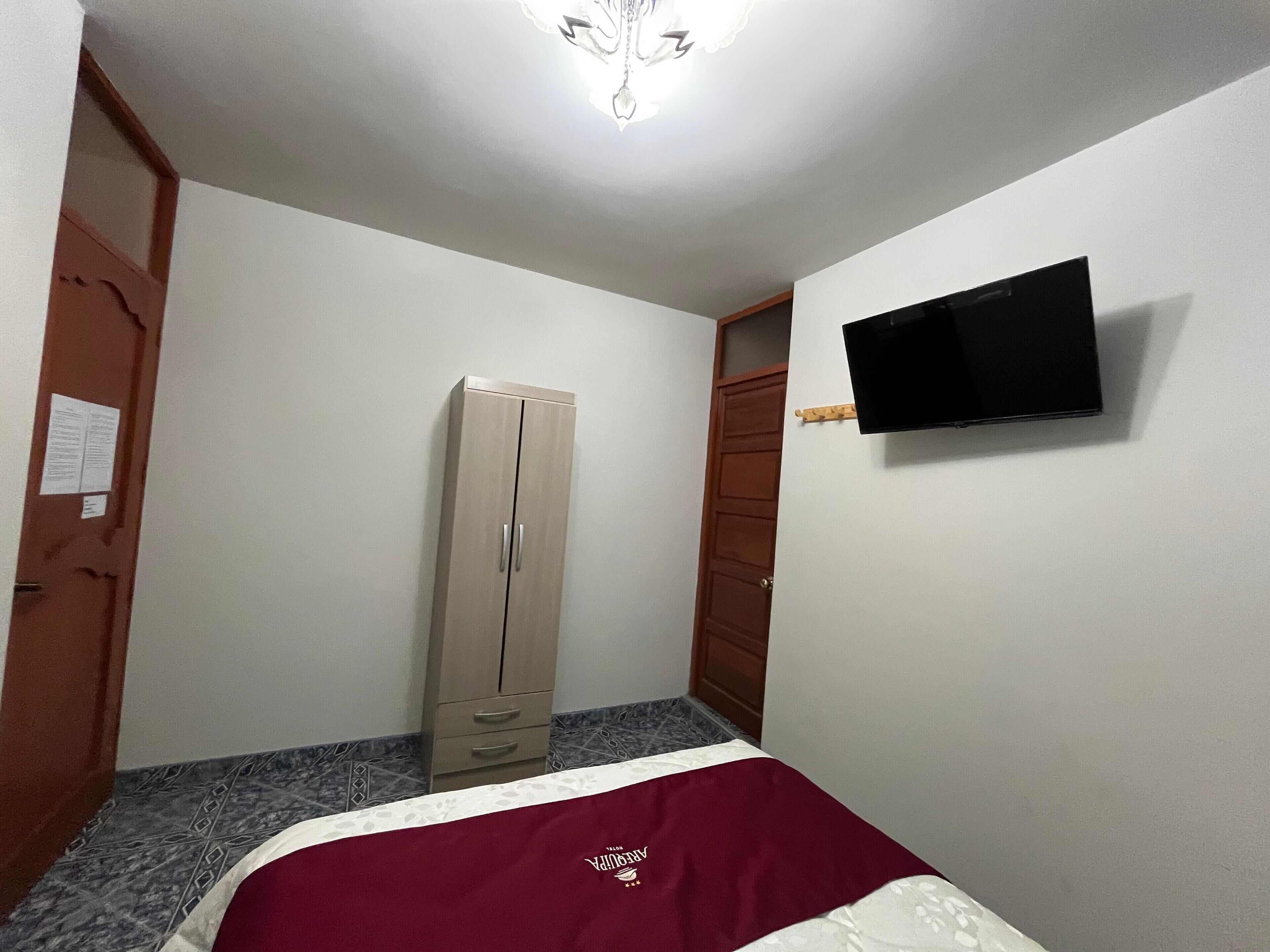 Quarto com cama, guarda-roupa, televisão e porta.