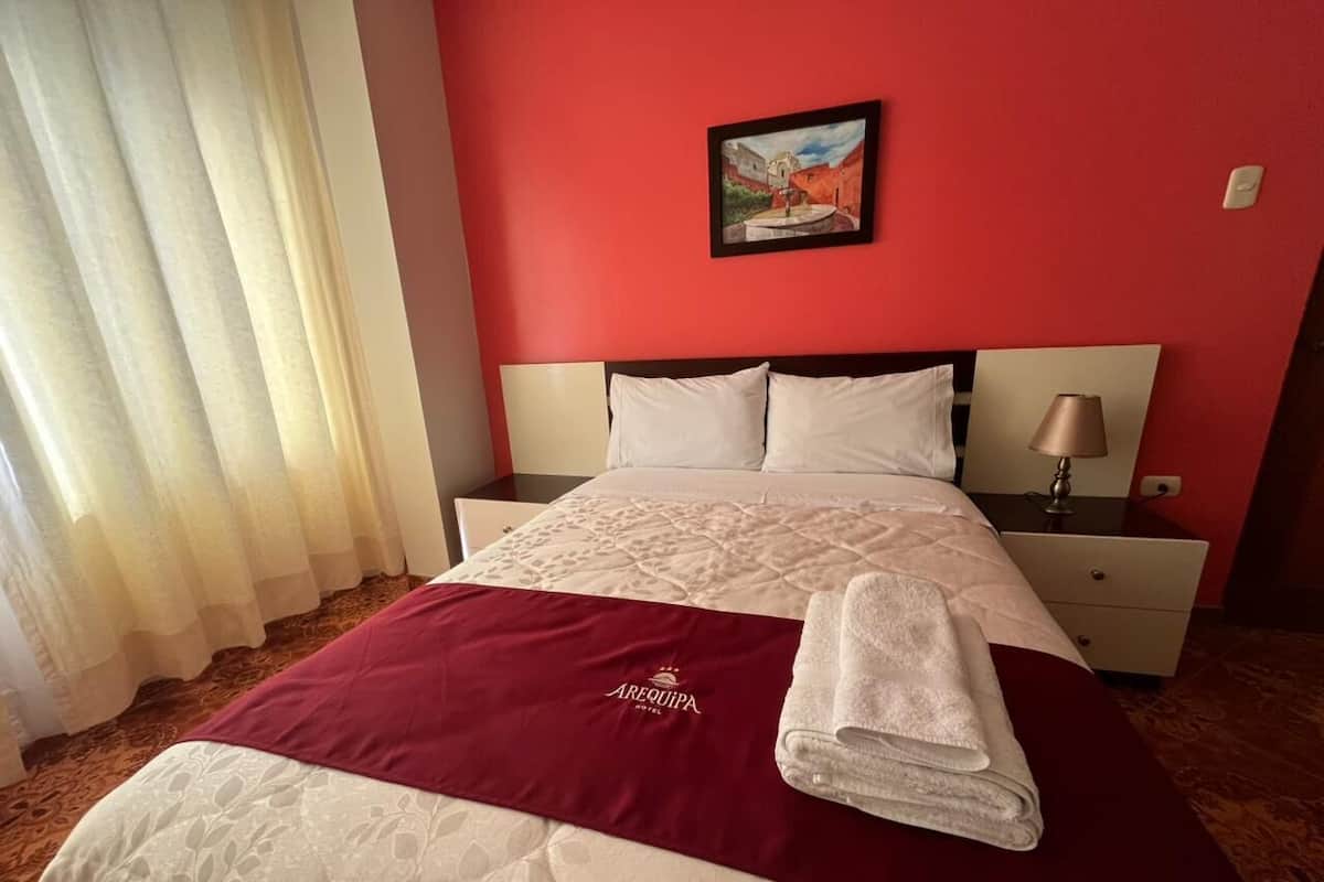 A hotel room with a bed, a nightstand, a lamp, and a painting on the wall.