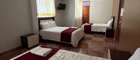 Una habitación de hotel con dos camas, un televisor montado en la pared y una mesita de noche.