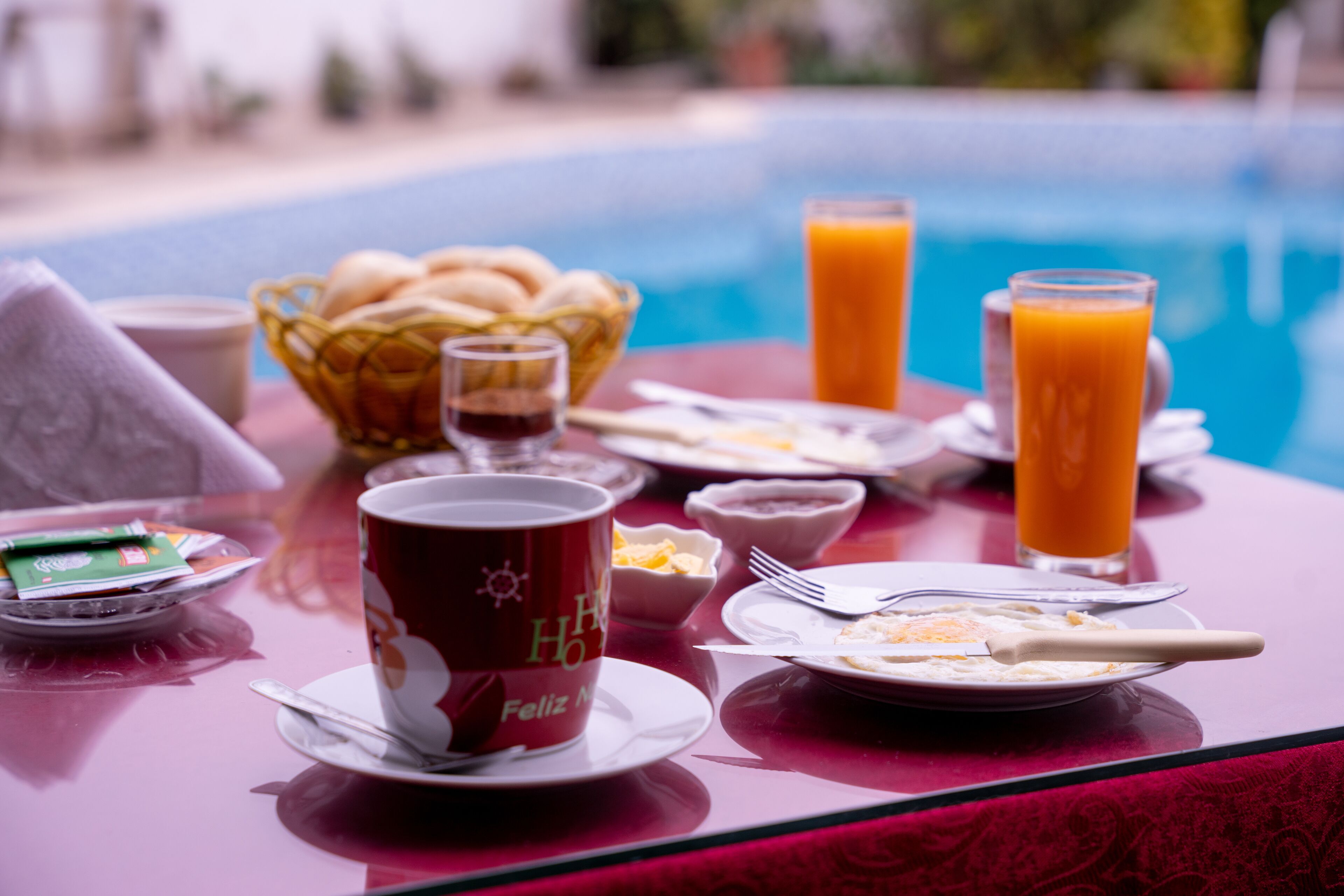 A breakfast table with a pool view, including a bowl of fruit, a cup, and a glass of orange juice.