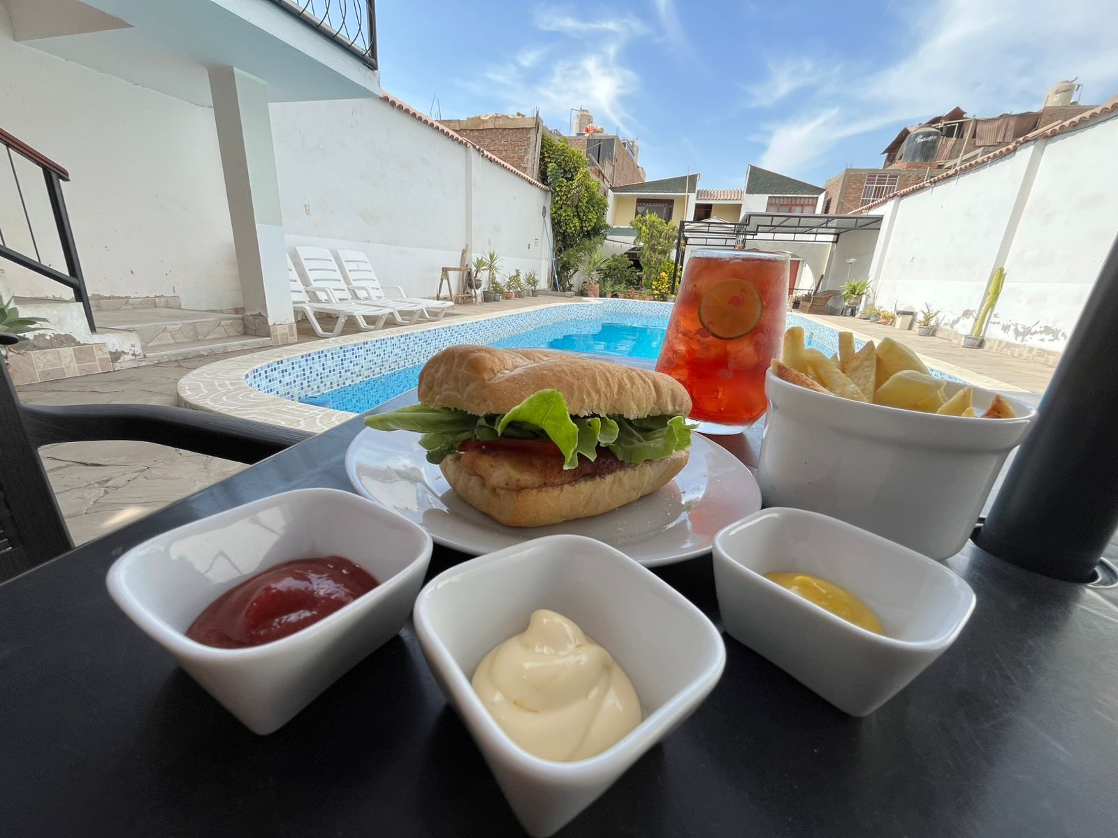 Ett matbord med en smörgås, ketchup, senap och en dryck med en citronskiva.