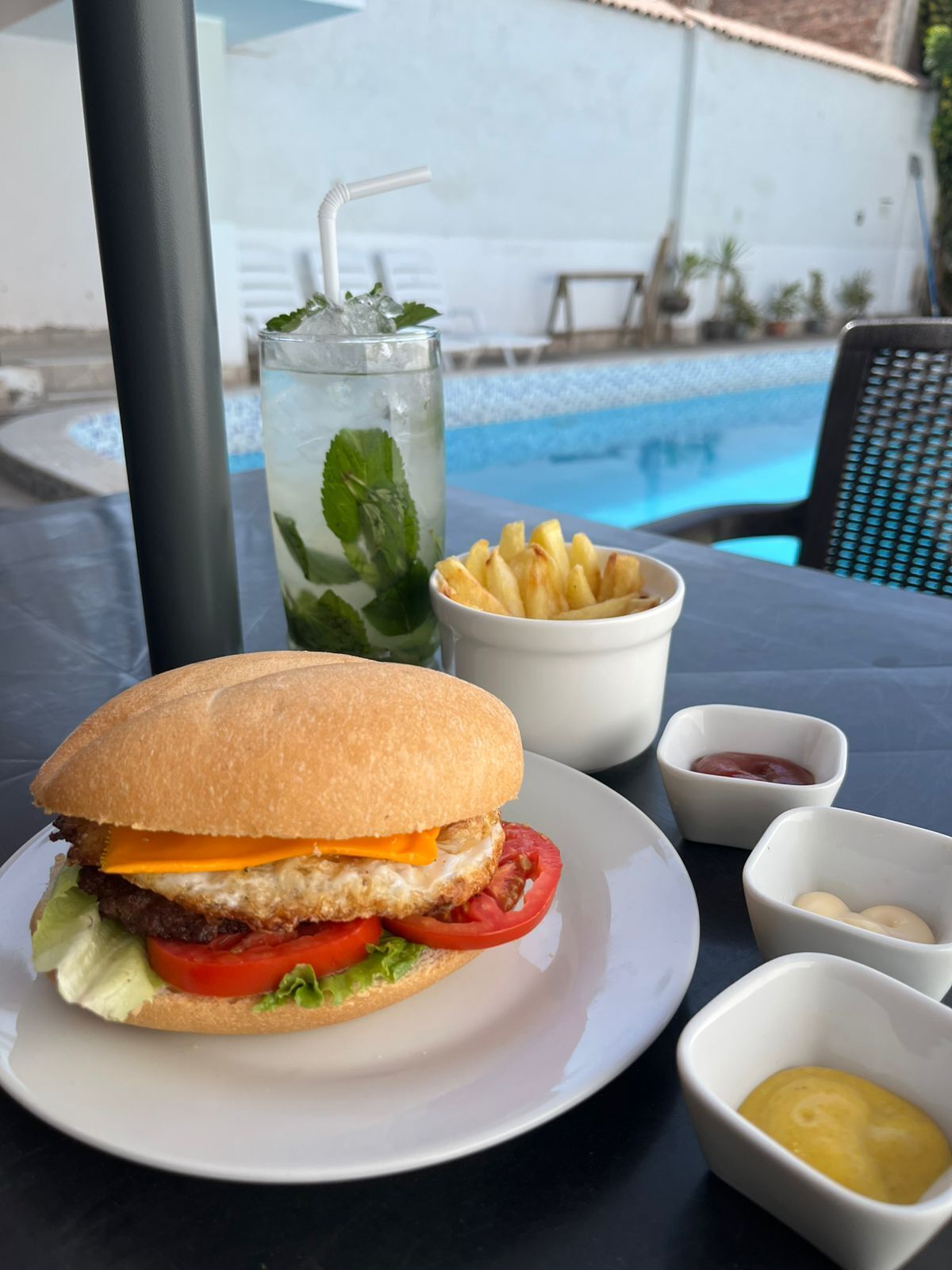 Un pasto con hamburger, patatine fritte e una bevanda, su un tavolo vicino a una piscina.