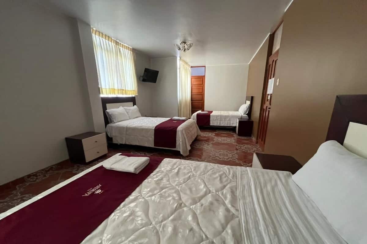 A hotel room with two beds, a TV, a wardrobe, and a window with curtains.