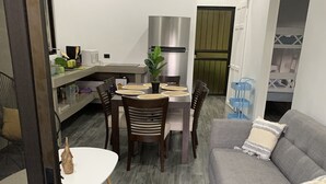 Een moderne woonkamer met een grijze bank, een eettafel met stoelen, een keuken met een roestvrijstalen koelkast en een welkomstmat.