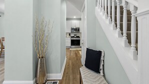 A hallway with a wooden floor, a white bench, a vase with branches, and a staircase with white balusters. - Stay in the heart of  Oakley (Cincinnati)