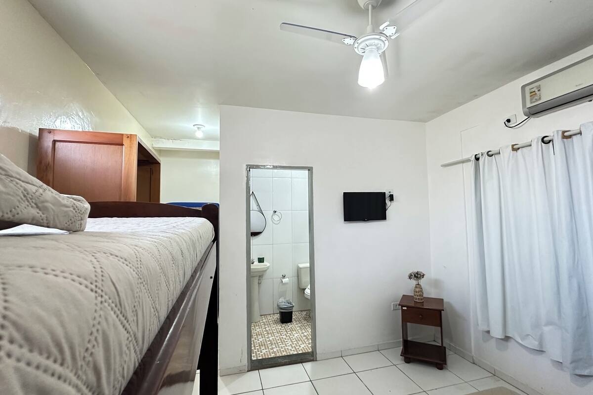 A bedroom with a bed, a ceiling fan, a bathroom with a toilet, and a shower curtain.