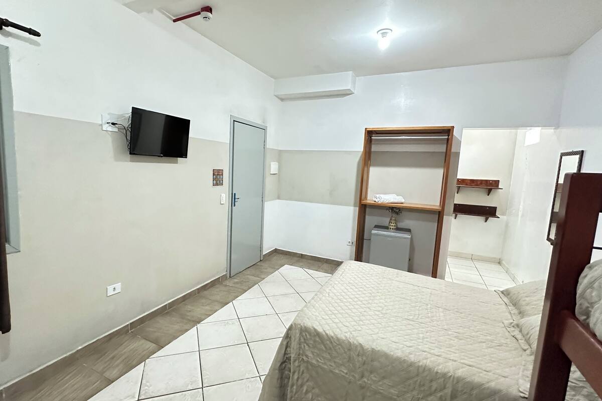 A bedroom with a bed, a wardrobe, a television, and a small refrigerator.