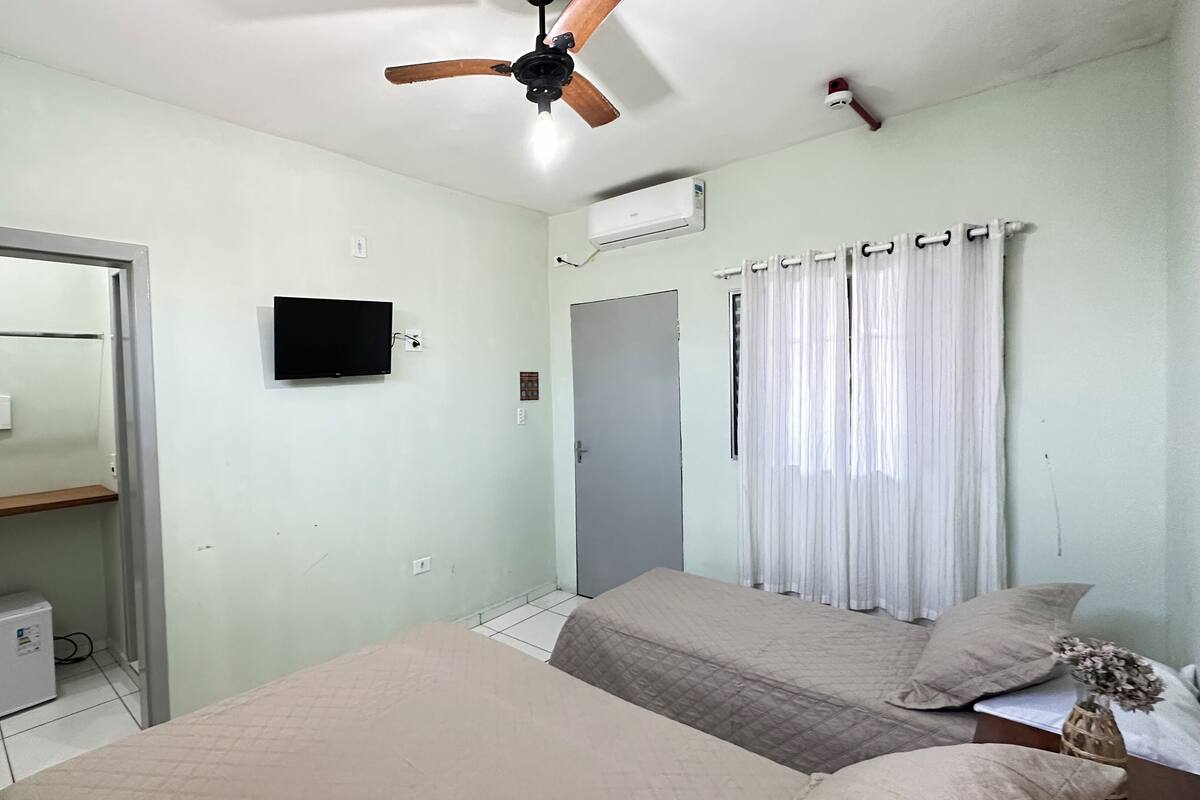 A bedroom with a bed, a ceiling fan, a TV, a wardrobe, and a window with curtains.