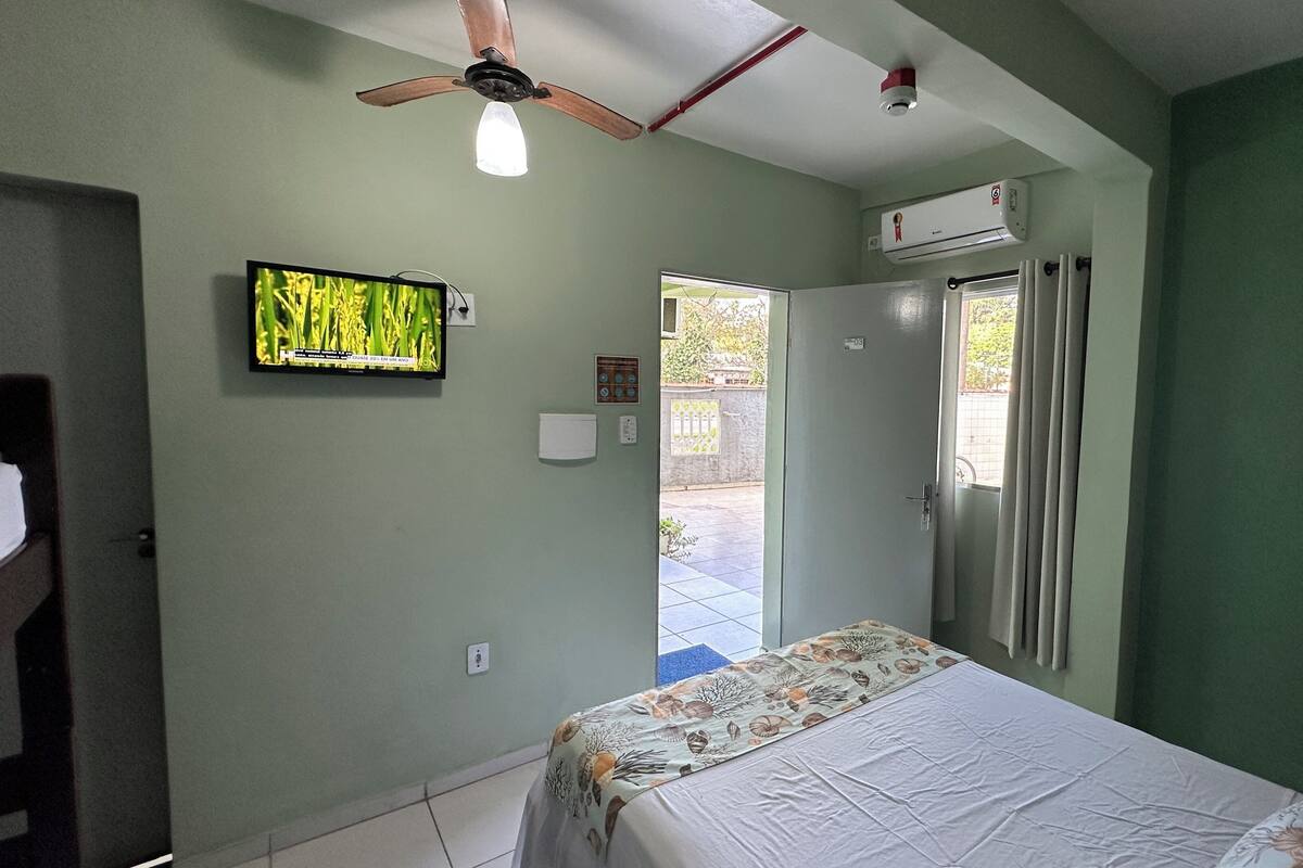 A bedroom with a bed, a ceiling fan, an air conditioning unit, a television, and a door leading to an outdoor area.