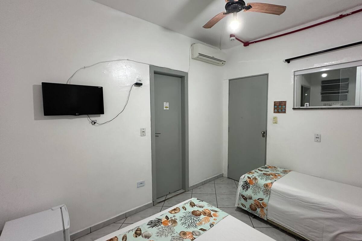 A small, clean room with two beds, a television, and a ceiling fan.
