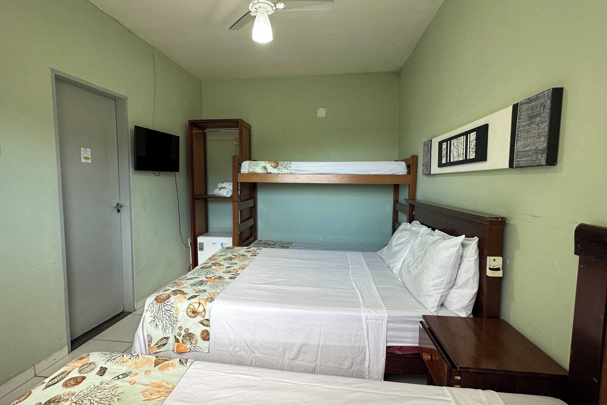 A single bedroom with a bunk bed, a bedside table, a ceiling fan, and a wall-mounted TV.