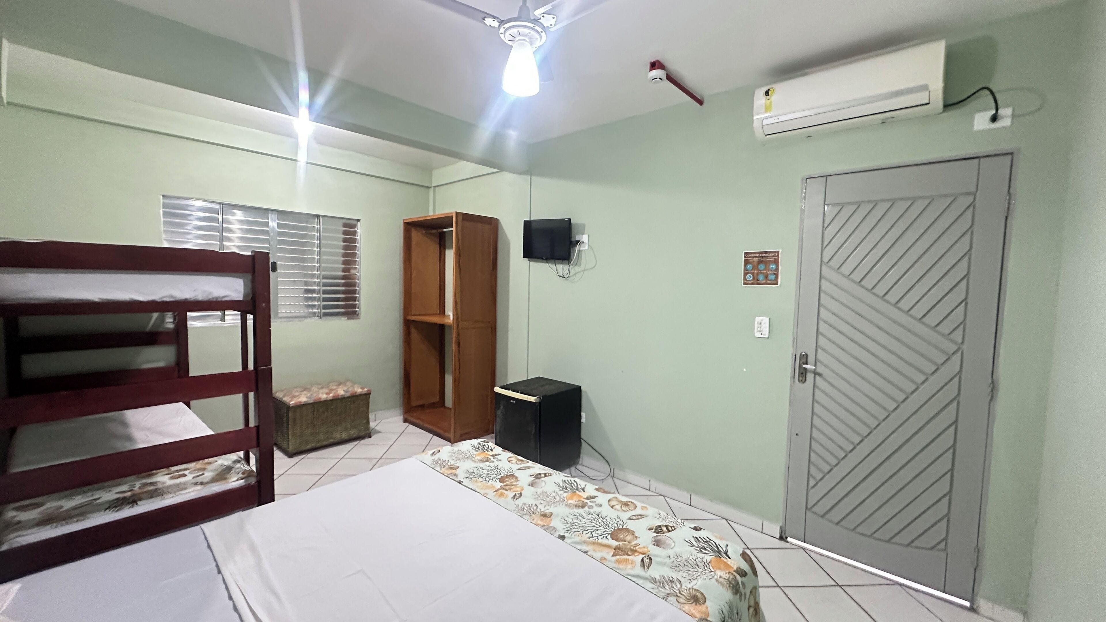 A room with bunk beds, a television, an air conditioner, and a door with a security lock.