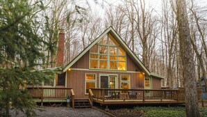 Une cabane dotée d’une terrasse en bois, de grandes fenêtres et d’une cheminée.