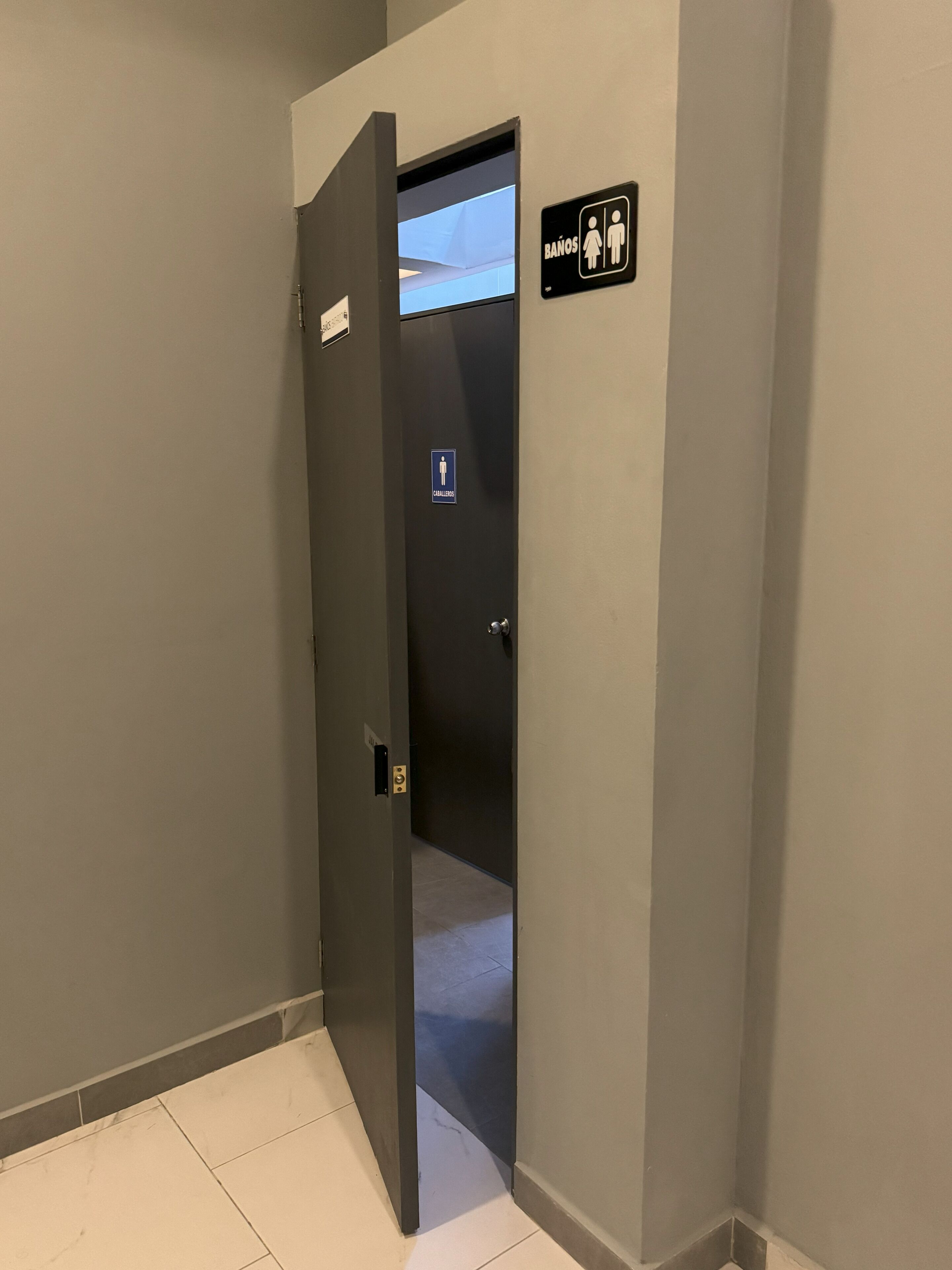 A hotel room entrance with a door leading to a bathroom, a sign indicating a men's and women's bathroom, and a visible towel rack.