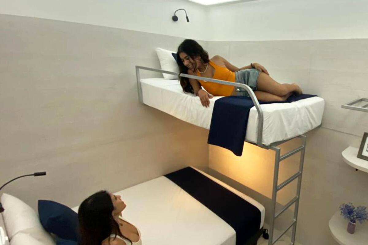 Een kleine, compacte kamer met een stapelbed, een enkel bed, een witte bank, een klein tafeltje met een vaas en een wandplank.
