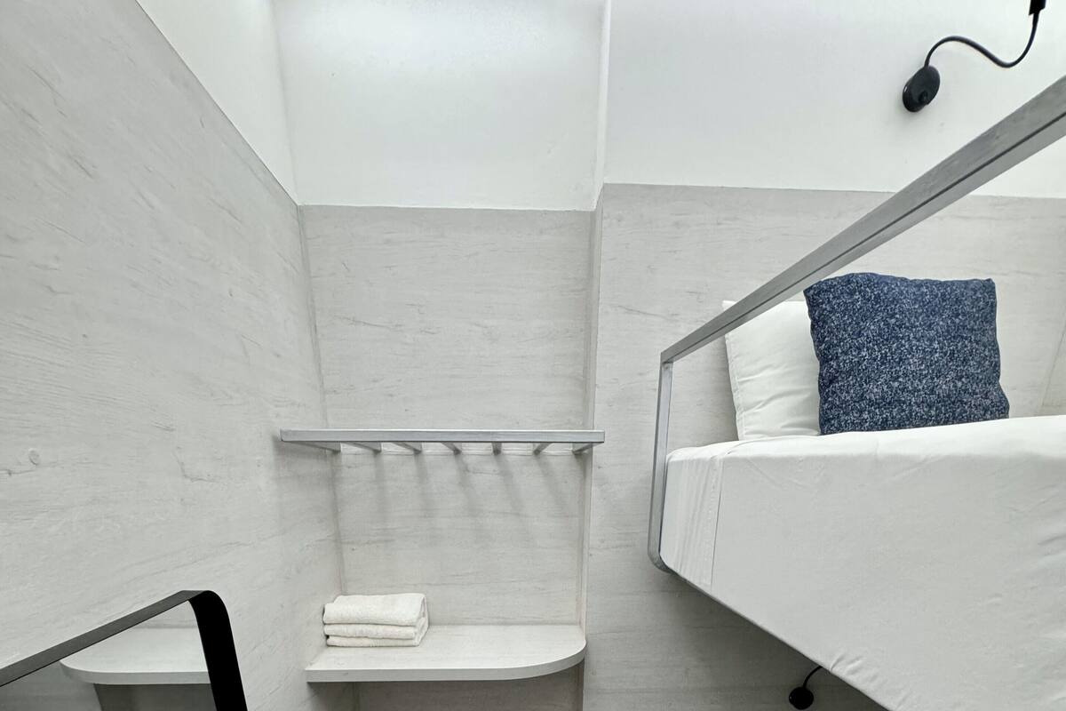 Een compacte, moderne badkamer met een douche, toilet en wastafel. Er staan twee stapelbedden met wit beddengoed en een donkig kussen.