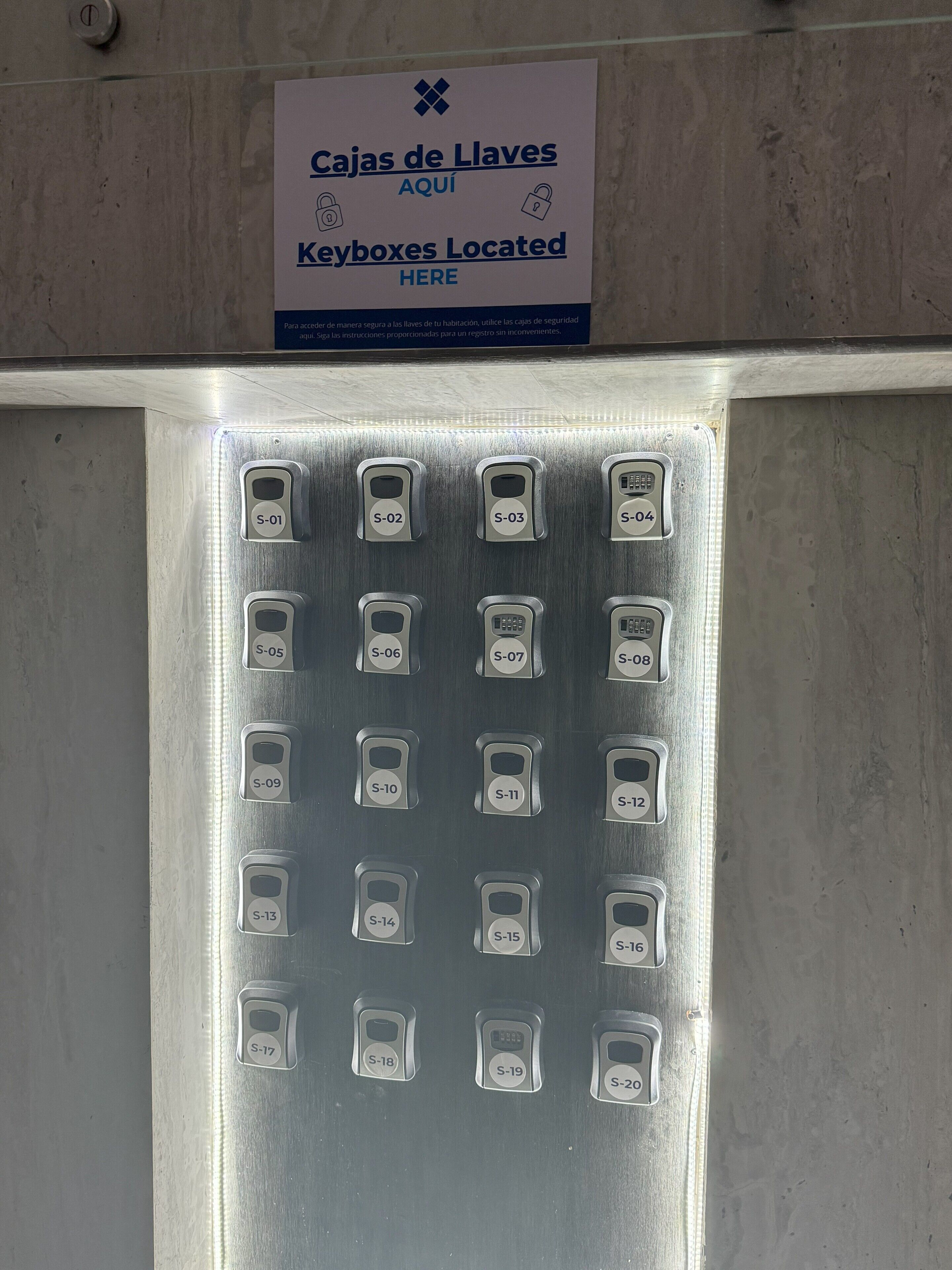 Un ascensor con botones de llamada numerados y un cartel que indica la ubicación de cajas de llaves.