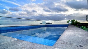 Une piscine sur le toit offrant une vue dégagée sur les gratte-ciel de la ville et un ciel nuageux.