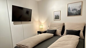 A modern bedroom with a bed, a TV mounted on the wall, and a framed picture above the bed. - Wunderschöne Wohnung in Kempten - Stadtmitte (Kempten (Allgäu))