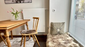 A cozy room with a wooden dining table, a chair, a fluffy rug, a radiator, a power outlet, and a window with blinds. - Wunderschöne Wohnung in Kempten - Stadtmitte (Kempten (Allgäu))