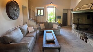 Un vaste salon doté d’une cheminée en pierre, d’un canapé, d’une table basse et d’un escalier menant à un autre niveau.