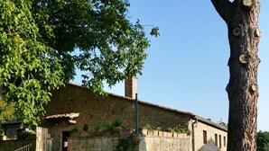 Un bâtiment rustique en pierre, doté d’un escalier en bois menant à une porte, entouré d’une zone herbeuse et d’une clôture en bois.