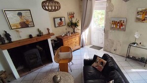 Un salon avec un canapé en cuir noir, une table basse en osier, une cheminée et un coin repas comprenant un buffet en bois et un luminaire suspendu.