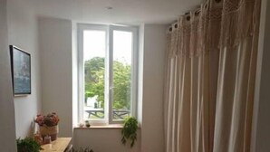 Une pièce étroite avec un plancher en bois, une table à manger entourée de chaises, une fenêtre avec des rideaux et un tapis tissé.