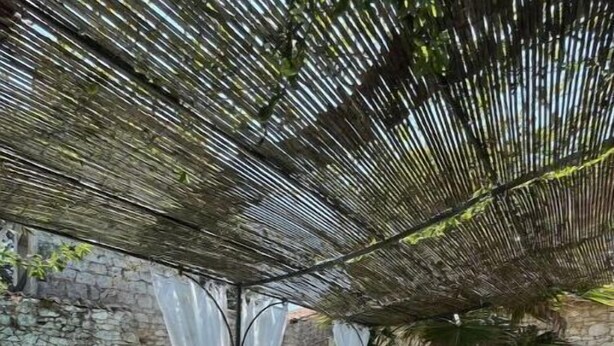 Une terrasse extérieure avec une table dressée pour le repas, une piscine et un mur de pierres en arrière-plan.