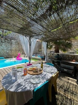 Un patio exterior con una mesa lista para comer, una piscina y un muro de piedra al fondo.