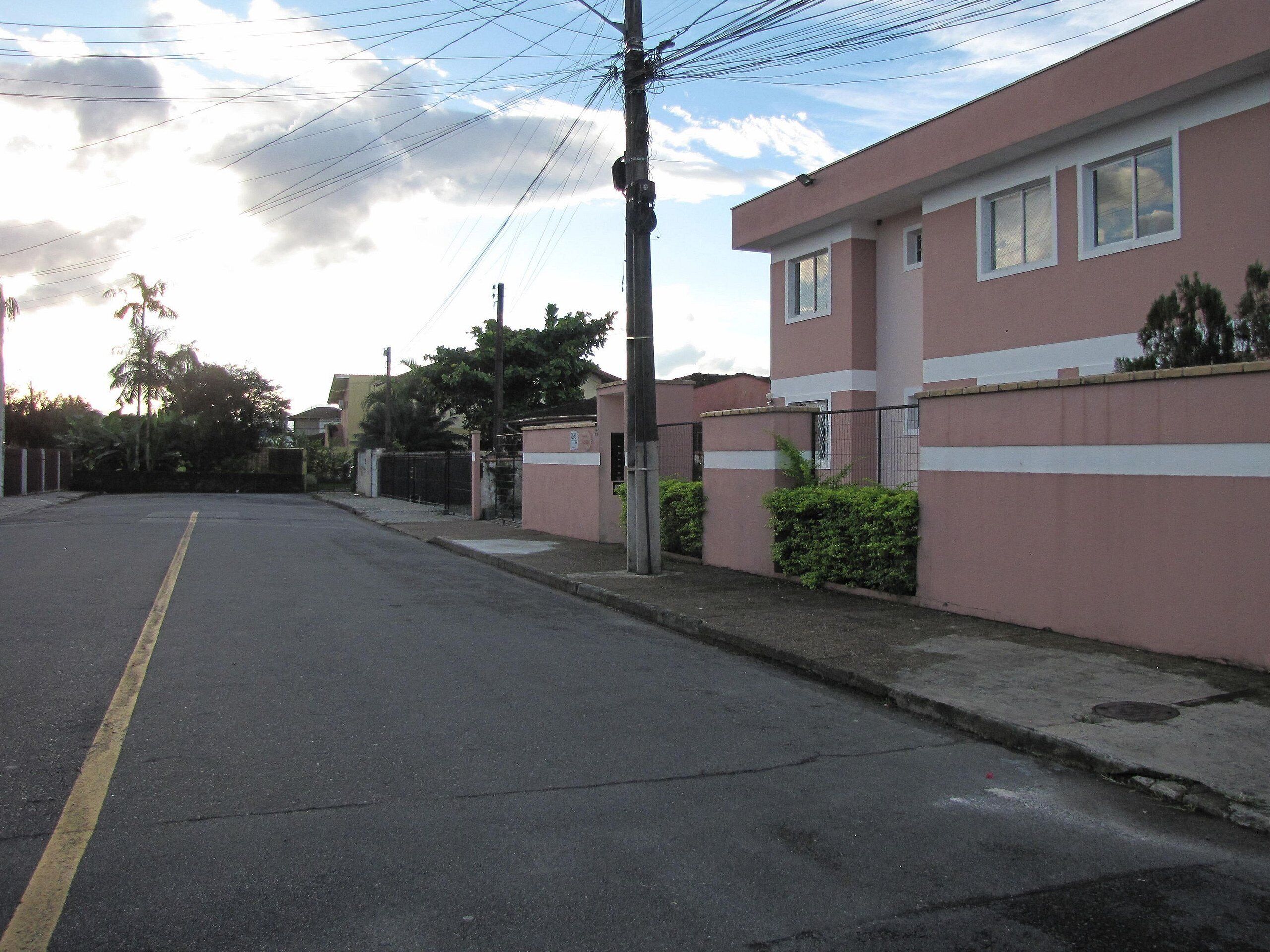 A residential street with a pink building, a clear road, and a utility pole.