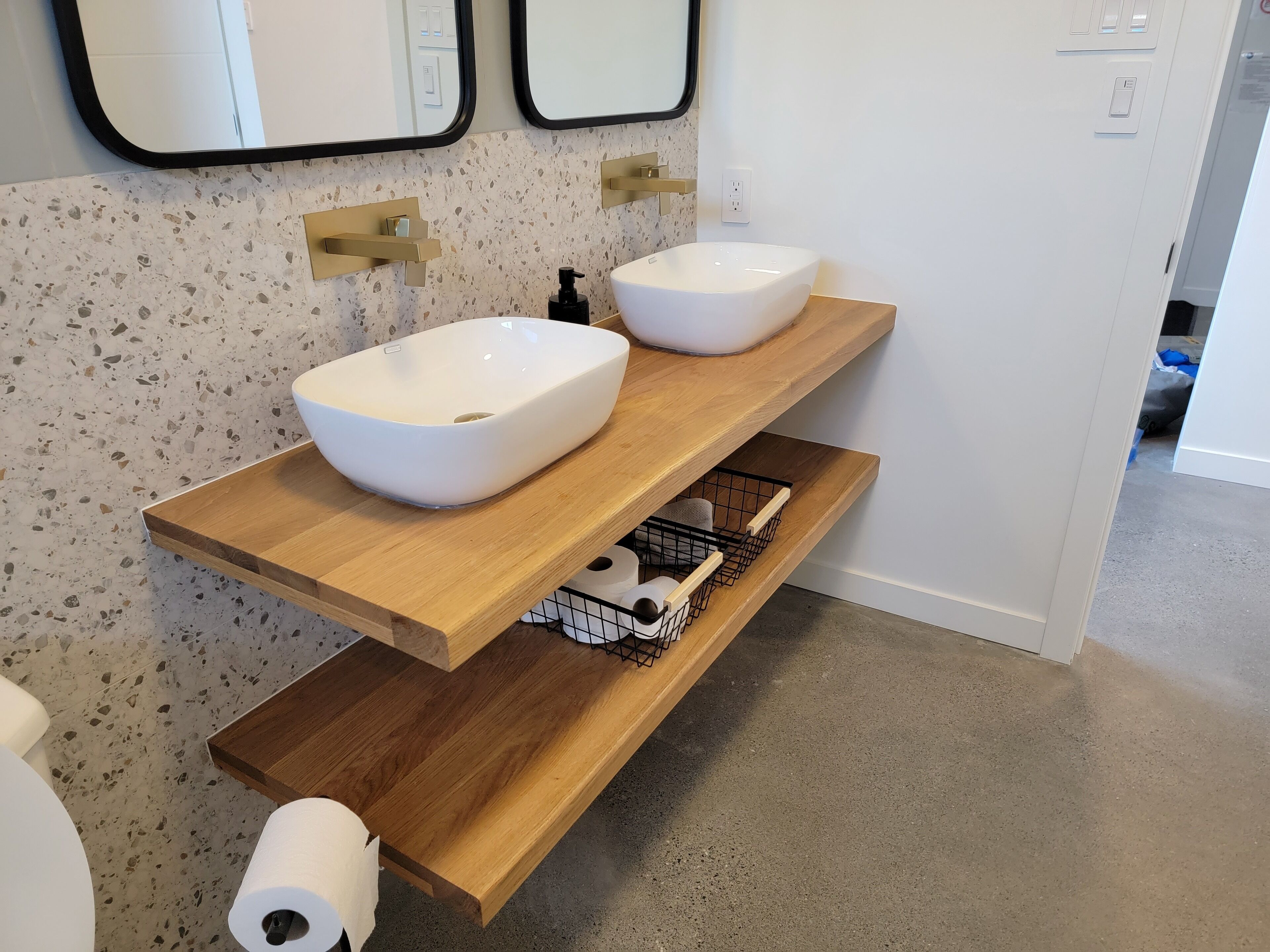 Une salle de bain avec deux vasques blanches, des étagères en bois et un pare-feu tacheté.