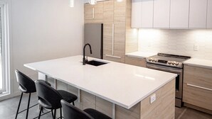 Una cucina moderna con isola centrale, sgabelli da bar, illuminazione a sospensione ed elettrodomestici in acciaio inossidabile.
