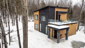 Ein modernes, zweistöckiges Haus mit Balkon, umgeben von einem verschneiten Wald.