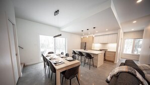 Una cucina moderna con un'isola centrale, una zona pranzo con un tavolo lungo e sedie, e un angolo salotto accogliente con un divano e una coperta.