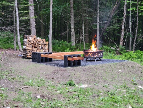 Un área de estar al aire libre con un pozo de fuego y un montón de leña.