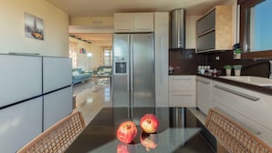 A modern kitchen with stainless steel appliances, a dining table with two chairs, and a view into the living area. - Villa Stefania (Chania)