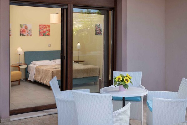 A hotel room with a bed, a small table with a vase of sunflowers, and white wicker chairs.