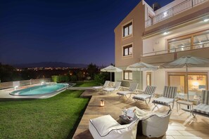 A modern outdoor pool area with lounge chairs and umbrellas, a well-maintained lawn, and a view of distant mountains. - Villa Stefania (Chania)