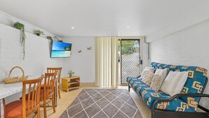 Un espacio habitable compacto con sofá, sillas, televisor y zona de comedor.