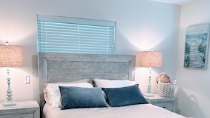 Un dormitorio con cama, dos mesitas de noche, un ventilador de techo y una ventana con persianas.