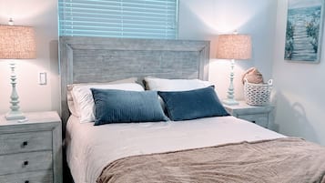 A bedroom with a bed, two bedside tables, a ceiling fan, and a window with blinds.