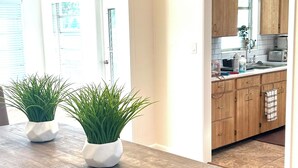 Un comedor con una mesa y sillas de madera, dos plantas en macetas y una lámpara de techo moderna.
