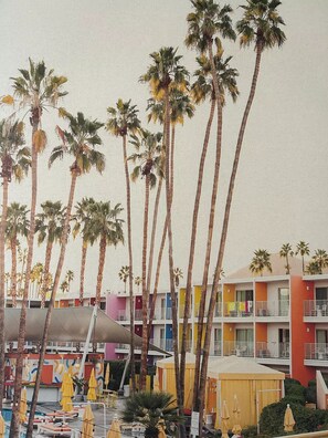 Een strandhotel met meerlaags gebouwen, palmbomen en een zwembad met ligbedden en parasols.
