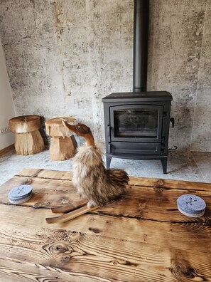 Ein rustikaler Raum mit Kaminofen, Holztisch und großem Stein.