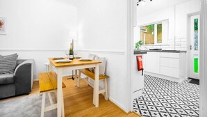 Un apartamento moderno con comedor, un sofá gris y una cocina con armarios blancos y suelo con estampado blanco y negro.